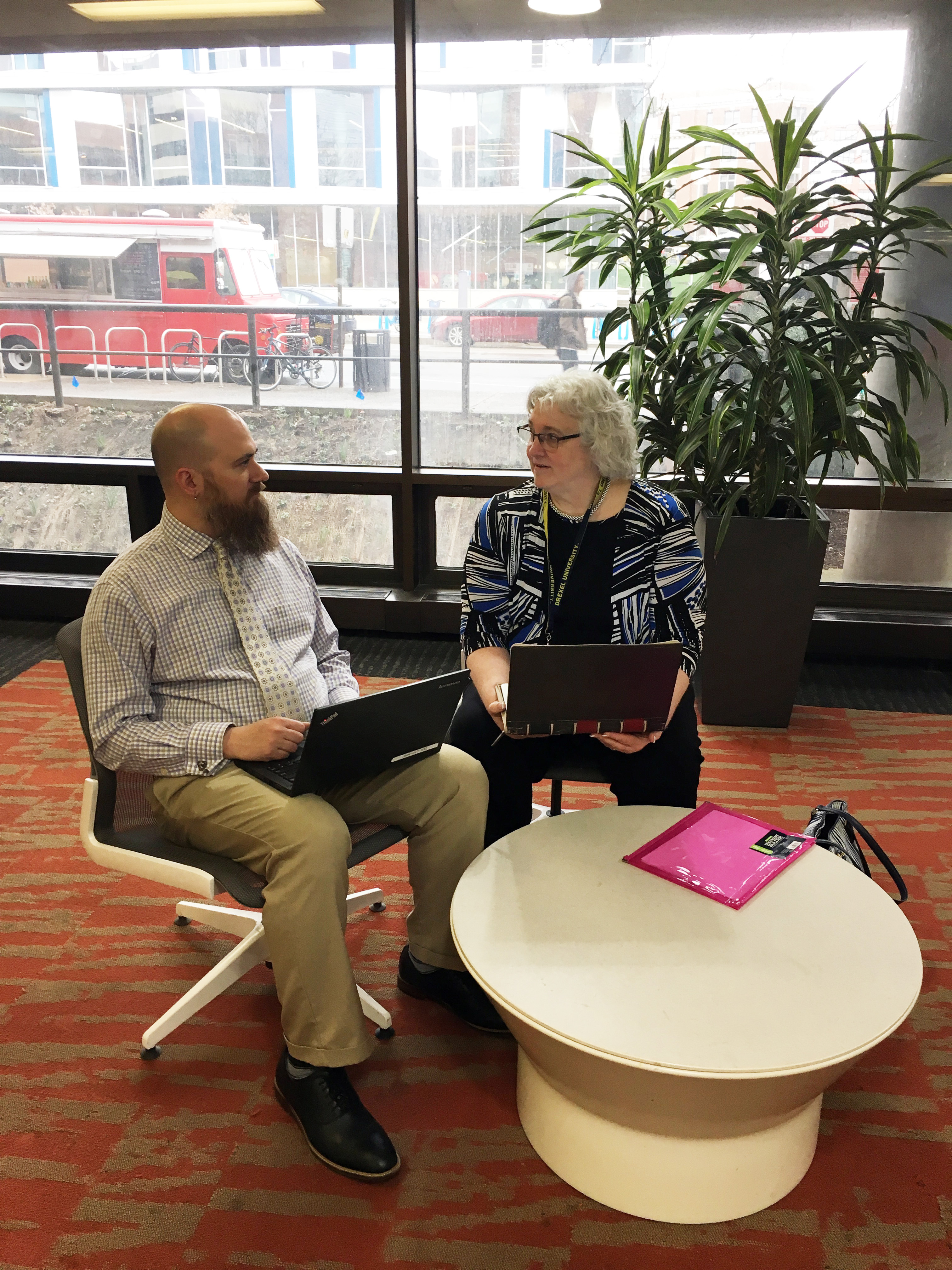 A man holding a laptop on his lap sits next to a woman who is also holding a laptop. 